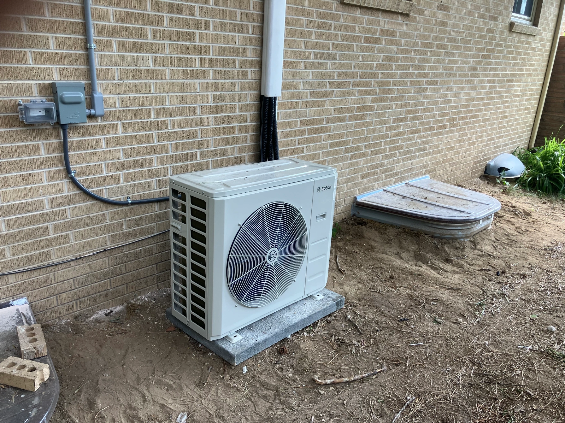 Professional Bosch heat pump installation on concrete pad with proper electrical connections and refrigerant lines